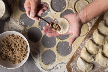 A man is making varenyky or dumplings, with meat, onions and bacon. Man is stuffing the dough with meat. Man in a black apron without face. Making dough by male hands at bakery Stone table close-up ph