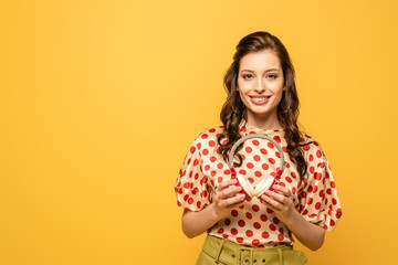 happy young woman smiling at camera while holding wireless headphones isolated on yellow