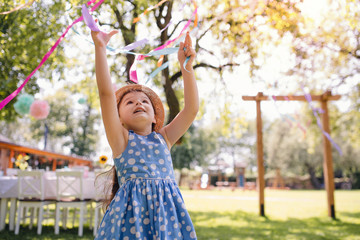 Small girl standing outdoors in garden in summer, birthday celebration concept.