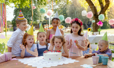 Down syndrome child with friends on birthday party outdoors in garden.