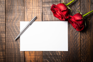 Red roses with a gift card to write on it on a wooden background. Concept of Valentine's Day, anniversary or mother's day.