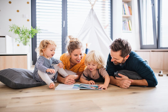 Young family with two small children indoors in bedroom reading a book.