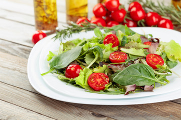Fresh mixed salad with cherry tomatoes on white plate.