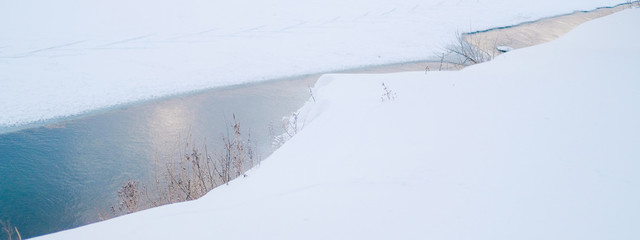 Thin ice melts on the river in early spring. Snowy riverbank with dry grass. Pure and clean nature...