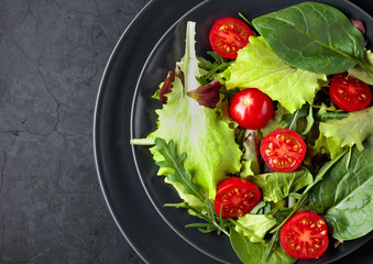 Fresh mixed salad with cherry tomatoes on a black background. Top view.
