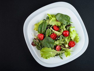 Fresh mixed salad with cherry tomatoes on a black background. Top view.