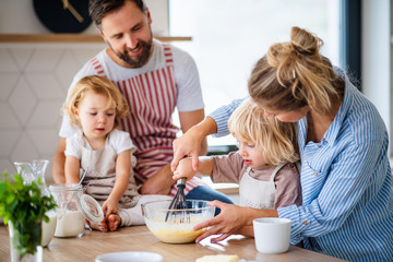 Young family with two small children indoors in kitchen, cooking.