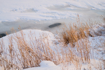 Thin ice melts on the river in early spring. Snowy riverbank with dry grass. Pure and clean nature concept