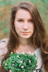Naklejka premium pretty girl holding white spring flowers walking through the green forest