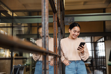 Fototapeta premium Image of young asian woman holding cellphone while working in office