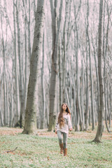 pretty young girl with long hair walking through the green forest in the spring