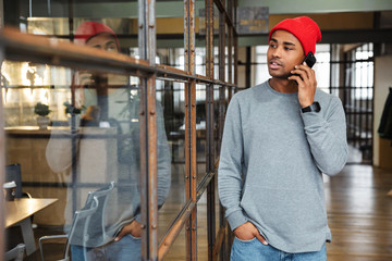 Image of young african american man talking on cellphone in office