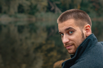 A guy with a beard sits on the lake and smokes an electronic cigarette. Blows puffs of smoke. The concept of unity with nature. Rest near the water. Vape, Man Vaping. lips and smoke, a lot of smoke.