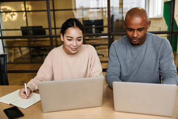 Image of multiethnic young coworkers working on laptops in office