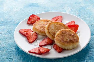 Pancakes with cheese and strawberries. Cheesecakes with strawberries and cream. Pancakes are served on a blue table. Great for breakfast. Close-up shot. Free space for text.