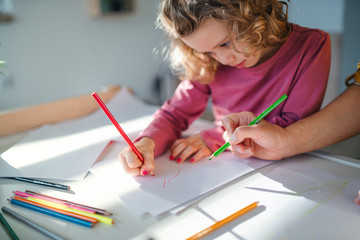 A cute small girl with mother indoors at home, drawing pictures.