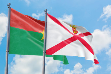 Jersey and Burkina Faso flags waving in the wind against white cloudy blue sky together. Diplomacy concept, international relations.