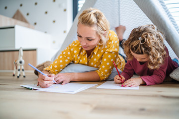 A cute small girl with mother indoors at home, drawing pictures.