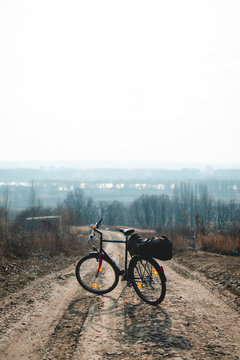 Outdoor view on bicycle with things, a tent on the trunk.. hilltop overlooking a valley in haze, a city on the horizon. winter or autumn landscape dirt road. vertical photo
