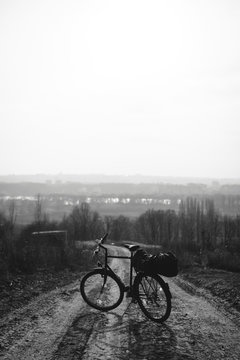 Outdoor view on bicycle with things, a tent on the trunk.. hilltop overlooking a valley in haze, a city on the horizon. winter or autumn landscape dirt road. vertical photo black and white