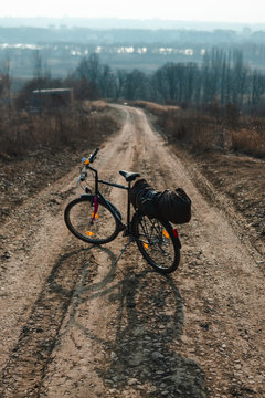 Outdoor view on bicycle with things, a tent on the trunk.. hilltop overlooking a valley in haze, a city on the horizon. winter or autumn landscape dirt road. vertical photo