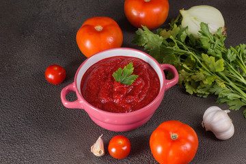 Tomato soup with parsley, onion and garlic on gray background. Comfortable food. Rustic style..