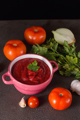 Tomato soup with parsley, onion and garlic on gray background. Comfortable food. Rustic style..