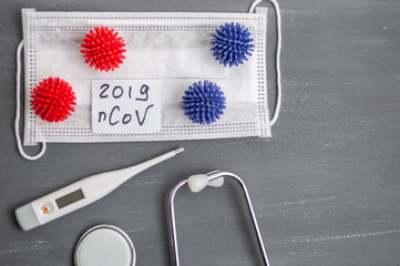 Medical face mask, stethoscope and digital thermometer with inscription Wuhan coronavirus 2019-nCoV on the gray table background. Novel coronavirus 2019-nCoV concept.