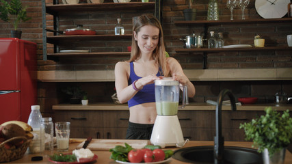 Close up rotation view of slim attractive young woman in trendy sportswear smelling cooked organic smoothie made in blender. Fresh, vegetables, fruits. Being on a diet, healthy food and nutrition