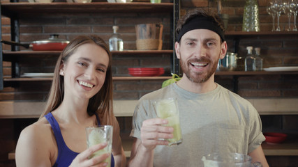 Young positive couple of vegetarians, sportsmen cheering up and drinking fresh smoothie on the kitchen at home. Gorgeous fit woman rubbing her stomach. Diet, healthy eating, fitness lifestyle, proper