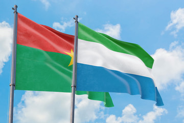 Sierra Leone and Burkina Faso flags waving in the wind against white cloudy blue sky together. Diplomacy concept, international relations.
