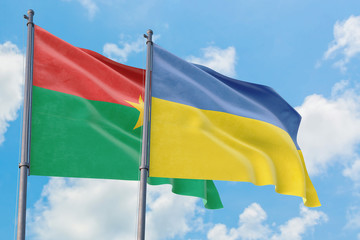Ukraine and Burkina Faso flags waving in the wind against white cloudy blue sky together. Diplomacy concept, international relations.
