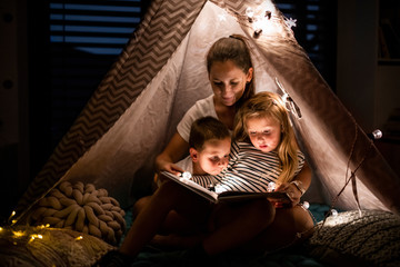 Mother with children sitting indoors in bedroom, reading a book.