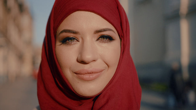 Close-up Portrait Of Wonderful Muslim Young Lady In Red Hijab Smiling At Camera Staying In The City Park.