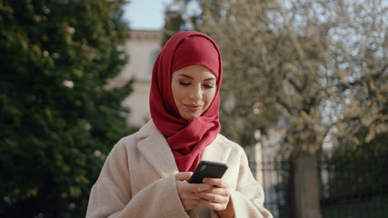 Attractive arab sociable young woman using a smatphone outdoors. Busy lovely Muslim girl with mobile phone.