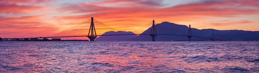 Sunset view on the bridge near Patras. Suspension bridge crossing Corinth Gulf strait, Greece, Europe. Second longest cable-stayed bridge in the world. Dramatic red sky under a Rion-Antirion Bridge.