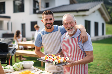 Portrait of father and son outdoors on garden barbecue, grilling. - obrazy, fototapety, plakaty