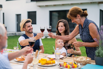 Portrait of family with wine sitting at table outdoors on garden barbecue.