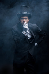 thoughtful magician in suit and hat standing in dark smoky room