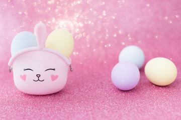 Easter bunny bag with eyes, nose, mouth with colorful eggs: purple, yellow and blue on a pink sparkling background. The hare is a symbol of a religious holiday and Catholics, Orthodox and Protestants