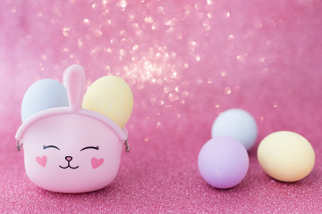Easter bunny bag with eyes, nose, mouth with colorful eggs: purple, yellow and blue on a pink sparkling background. The hare is a symbol of a religious holiday and Catholics, Orthodox and Protestants