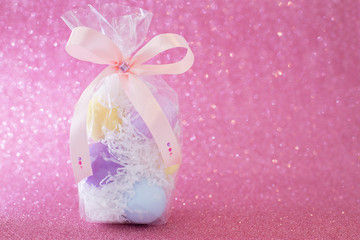 Multi-colored purple, pink, blue, yellow Easter eggs in a transparent gift package, decorated with a bow and rhinestones, on a pink shiny bokeh background. Symbol of celebration of religious holiday