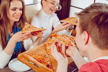 The company of guys in the pizzeria. Cheerful guys with pizza in their hands. Students in a cafe