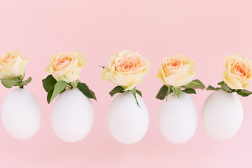 Bushy beige, yellow,orange roses in Easter white eggshell flying in the air on light pink background. Eggs are symbol of celebration of a religious holiday among Catholics, Christians and Protestants