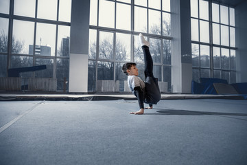 Fototapeta na wymiar Little male gymnast training in gym, flexible and active. Caucasian fit little boy, athlete in sportswear practicing in exercises for strength, balance. Movement, action, motion, dynamic concept.