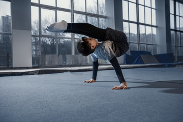 Fototapeta na wymiar Little male gymnast training in gym, flexible and active. Caucasian fit little boy, athlete in sportswear practicing in exercises for strength, balance. Movement, action, motion, dynamic concept.