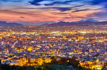 An evening cityscape of many buildings of Athens City, Greece. View from Filopappou Hill or Hill of the Muses. Colorful spring landscape. Urban skyscraper skyline rooftop view at night.