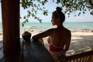 Young and sexy woman sitting in authentic beach bar with a coconut drink