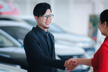 Handsome businessman in a suit enters into a car sale agreement with a saleswoman and shakes hands at a new car showroom.