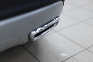 Chrome exhaust pipe of a modern new car. The background is blurred. The car is exhibited in the showroom